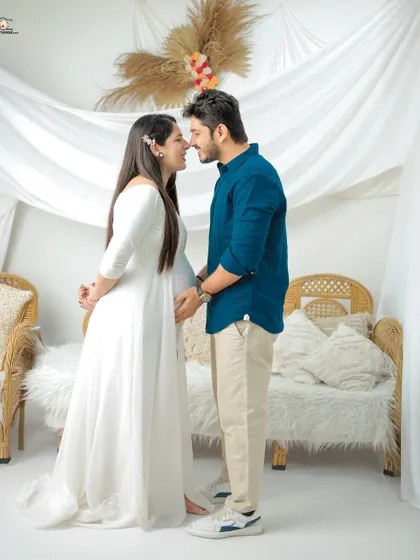 The couple shares a loving gaze in this bright studio shot. Dressed in white and blue, they stand close together, their expressions full of anticipation and happiness.