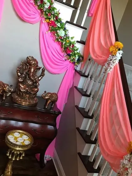 Staircase decoration for a home event, using bright pink drapes and floral arrangements. This adds a festive touch to every corner of the house.