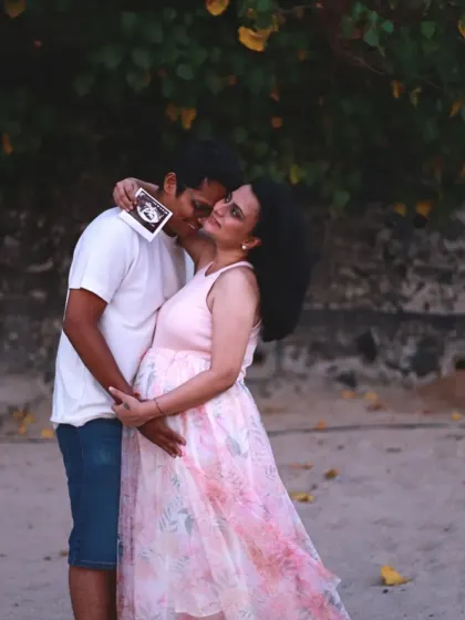 A truly special moment on the beach where the father-to-be kisses his partner's cheek while she holds up their baby's ultrasound picture.