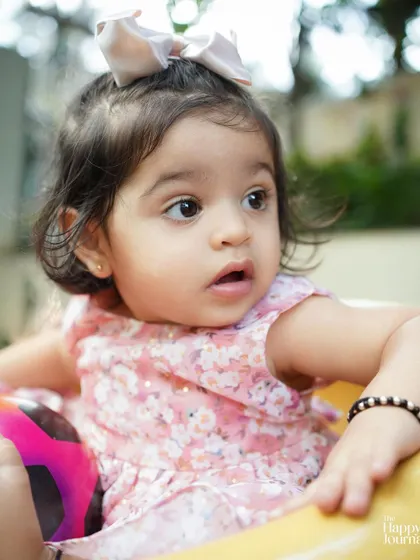 A close-up of a baby girl in a pink floral dress, looking with wide-eyed wonder. A beautiful capture of a baby's curiosity.