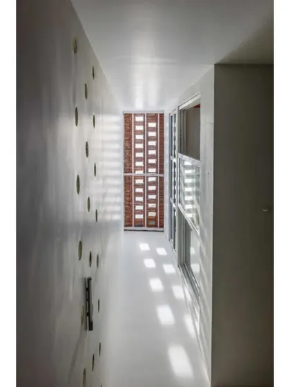 A narrow interior space is illuminated by light filtering through a perforated screen. This project is a masterclass in controlling natural light to create a serene and glare-free environment.