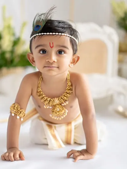 A full-body shot of a baby boy dressed as Krishna, crawling towards the camera. His determined expression and adorable costume make for a very cute and dynamic portrait.