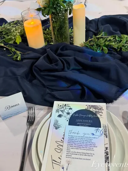 A close up of a single place setting from the blue and white dinner party. This view shows the personalized menu card, a custom place card for "Rionna," and the detailed floral and candle centerpiece.