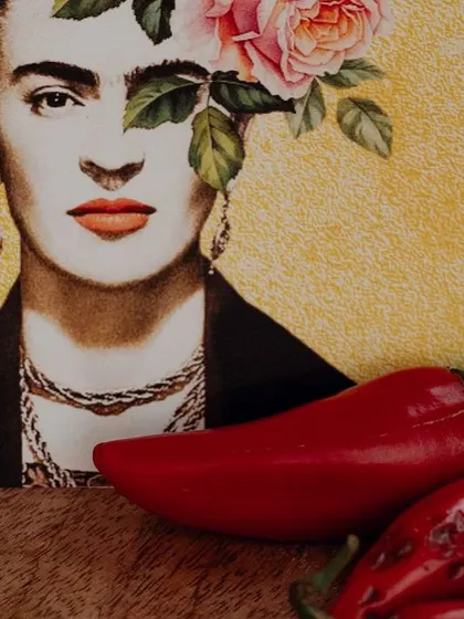 A close-up of a Frida Kahlo postcard and a red chili, showcasing the small, thematic details that bring the story to life.