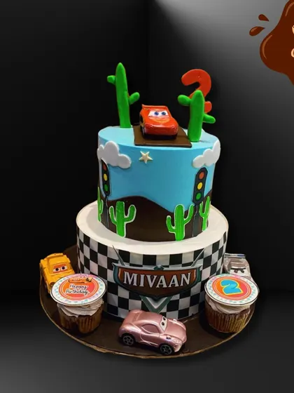 This two-tier Disney Cars cake is ready to race. It features a checkered flag base, cactus decorations, and Lightning McQueen on top, along with matching themed cupcakes on the side.