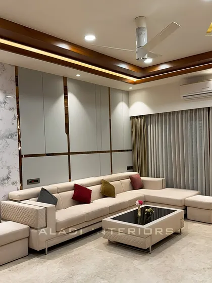 A luxurious living room with a large, comfortable sectional sofa in a neutral tone. The wall behind features clean white panels with elegant gold-colored inlays, adding a subtle touch of opulence.