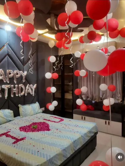 A stylish bedroom decorated for a birthday. The room features red and white ceiling balloons and a bed decorated with an 'I LOVE YOU' message made of rose petals.