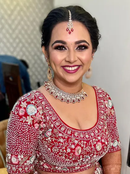 A radiant smile from a beautiful bride. Her look features soft smokey eyes and a lovely berry lip color, perfectly matching the embroidery on her red wedding lehenga.