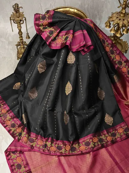 A classic black silk saree with a contrasting pink embroidered border. The gold leaf motifs on the body add a touch of timeless elegance to this beautiful piece.