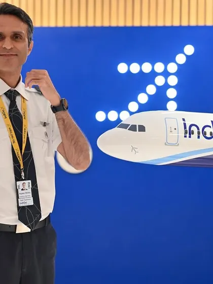 A confident pose from an IndiGo pilot. The composition uses the company logo and a model plane to reinforce the brand identity.