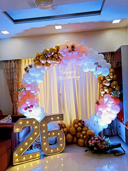 A beautiful circular balloon arch in pastel and gold tones for a 26th birthday. This home setup with a neon sign and marquee numbers creates a warm and celebratory atmosphere.