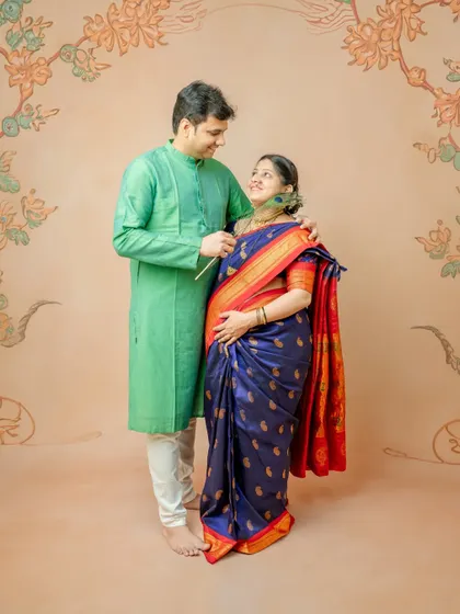 A playful and intimate moment between the couple. The husband gently touches his wife's chin with a peacock feather, bringing a smile to her face in this culturally rich maternity photo.