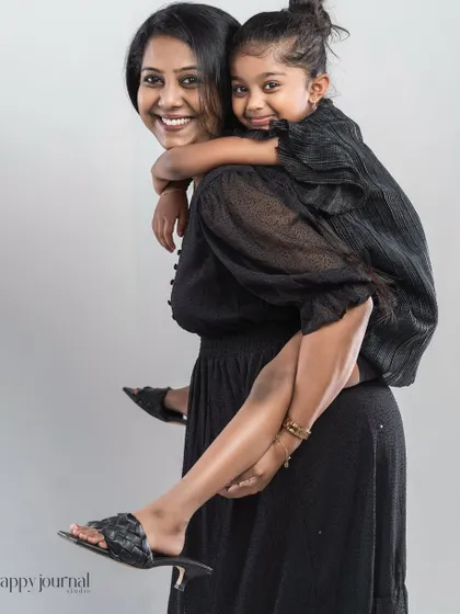 A mother gives her daughter a piggyback ride. Their matching black dresses and big smiles create a joyful and stylish portrait.