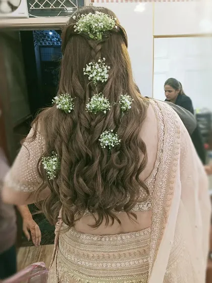 A beautiful half-up hairstyle with a fishtail braid and soft waves, adorned with baby's breath. This bohemian-inspired look is perfect for a Mehendi or outdoor wedding.