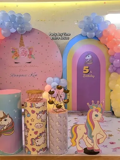 This unicorn decoration for a 5th birthday includes two backdrops, a rainbow arch, and themed plinths, creating a full scene for photos.