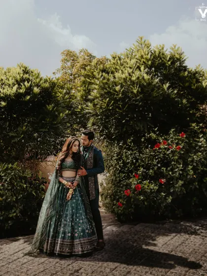 A duplicate of image 17, this wide shot captures a couple in coordinated dark green traditional outfits, standing in a lush garden, creating a stunning pre-wedding portrait.