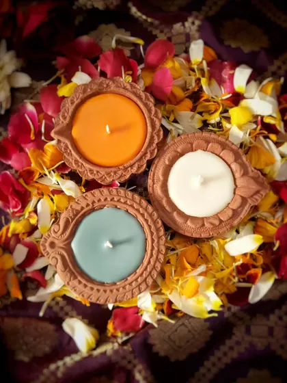 A top-down view of the tri-color Diya Candles nestled in a bed of flower petals. They are available scented or unscented to suit your preference for the celebration.