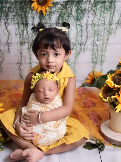 Dressed in matching yellow, this big sister holds her new baby sibling in a sunflower-themed shoot. Coordinating outfits can make family photos even more special.