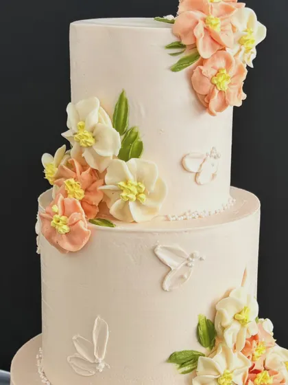A close-up of the delicate, handcrafted sugar flowers on a three-tiered engagement cake, showing the soft peach and cream tones.