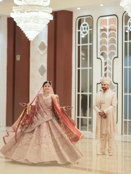 A joyful twirl from the bride as her groom looks on. This candid shot, set against the backdrop of a grand hall, captures the bride's happiness and the elegance of the celebration.
