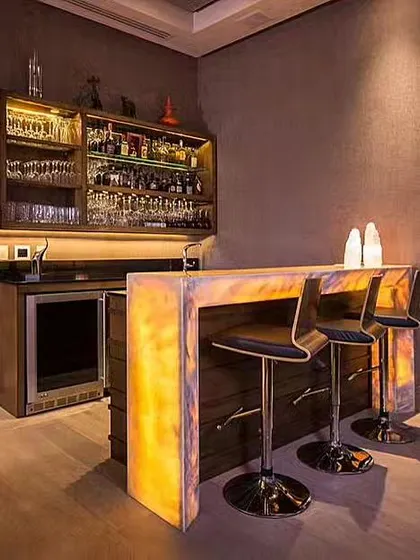 This luxurious home bar brings a warm, inviting ambiance with its sleek, backlit onyx counter. The soft, golden illumination creates a sophisticated glow, perfect for an upscale and intimate gathering space.