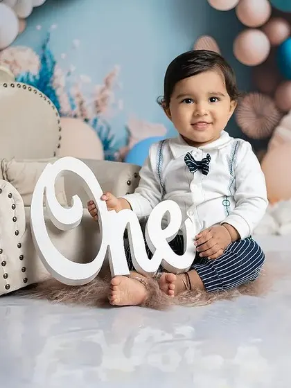 A classic first birthday portrait. This little boy is sitting proudly with a "One" sign in our pastel blue balloon-themed setup.