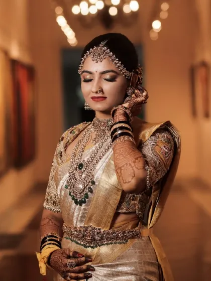 An artistic shot in a hallway, the warm lighting enhancing the golden tones of her saree and the intricate details of her jewellery.