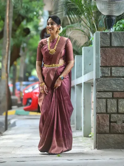 A full-length view of a graceful look for a family wedding. The makeup is kept elegant and fresh to complement her beautiful mauve silk saree and traditional gold jewelry.