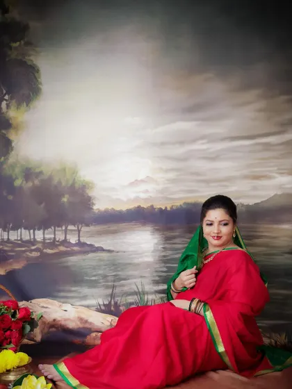 A serene portrait of a mom-to-be seated by a painted river backdrop. Her traditional red and green saree creates a beautiful, classic look.