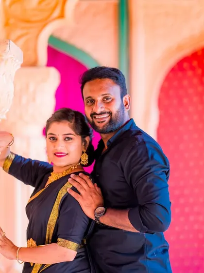 A close-up portrait of a couple in a vibrant, traditional setting. Their genuine smiles and the bright colors make this a very joyful and lively photo.