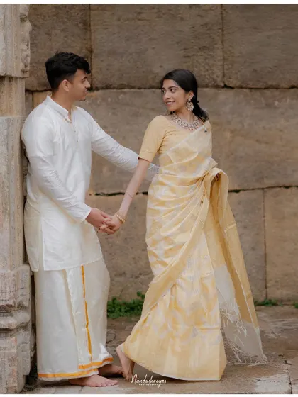 A couple holds hands by a stone wall, their traditional attire and gentle interaction creating a classic portrait.