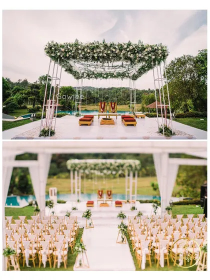 A modern and elegant outdoor mandap with a canopy of white flowers, set against a lush green backdrop.