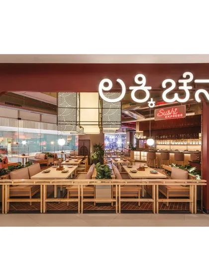 The exterior view showcases the restaurant's name in glowing Kannada script, grounding the international concept with a local touch. The open facade provides a welcoming glimpse into the lively interior.