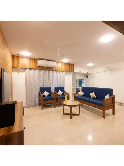 Here, a custom wooden sofa set with deep blue upholstery brings a pop of color and classic comfort. The space is designed to feel open and welcoming, with a unique wallpaper adding a touch of artistic flair.