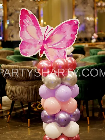 A close-up of a butterfly-themed balloon column centerpiece, showcasing a large pink watercolor butterfly prop that adds a beautiful, artistic touch to the tables.