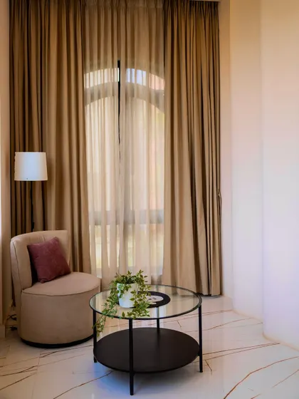 A quiet reading corner with an elegant armchair and floor-to-ceiling curtains that soften the light, creating a perfect spot for relaxation.