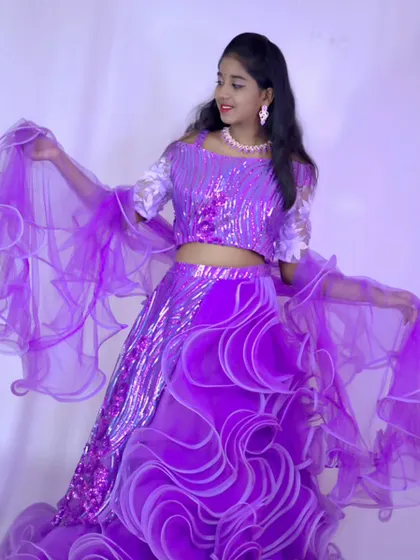 A playful shot of a young model showing off the flowing, ruffled dupatta of her purple sequin lehenga.