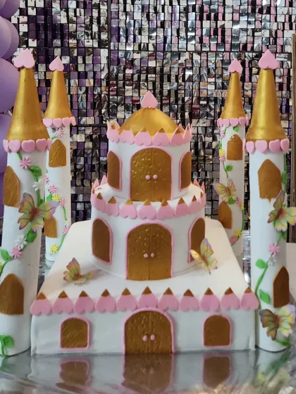 A close-up of a beautiful castle cake, with pink and gold details, turrets, and delicate butterfly accents. It's a fairytale dream come true.