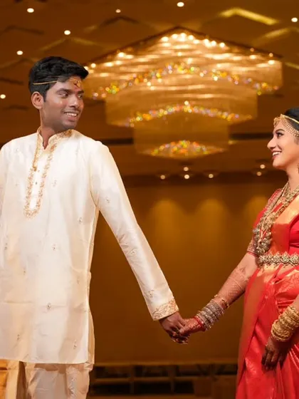 A happy shot of the couple holding hands and smiling at each other in a grand wedding hall.