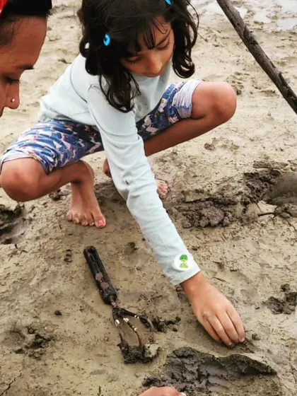 A close-up of a child's hands exploring the texture of the wet clay at the lake's edge.