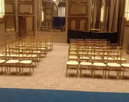 A simple and elegant seating arrangement for a reception or formal wedding event inside a modern hall, using classic Tiffany chairs.