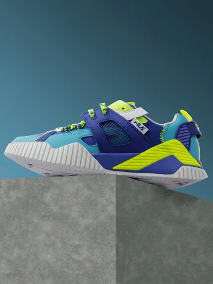A side profile of a vibrant, multi colored Fila sneaker, shot against a textured stone and a solid blue background.