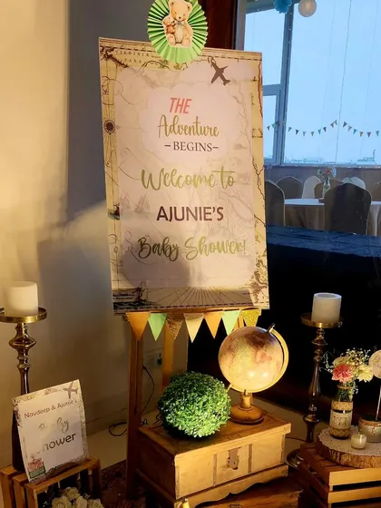The main welcome board for the baby shower. The vintage map design, combined with a globe, candles, and floral arrangements on wooden crates, creates a beautiful and thematic entrance.