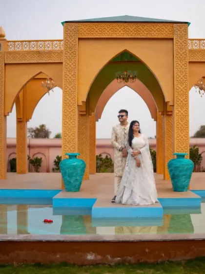 Standing together in a grand setting. This couple's matching white traditional outfits look absolutely regal against the stunning architecture.