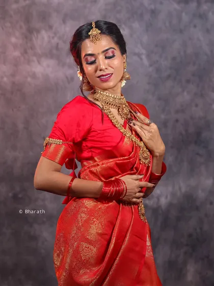 A studio session featuring a model in a vibrant red traditional saree. The mottled grey backdrop ensures the rich colors and gold jewelry stand out.