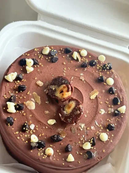 A decadent chocolate bento cake topped with Ferrero Rocher, chocolate chips, and gold sprinkles. A dream come true for any chocolate lover.