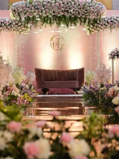 A beautiful reception stage bathed in soft pink light, with lush floral arrangements and circular floral chandeliers creating a dreamy atmosphere.