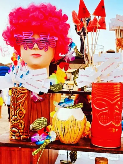 A quirky and colorful sundowner bar setup. The mannequin head with a pink wig and fun glasses is a playful centerpiece that gets people talking.