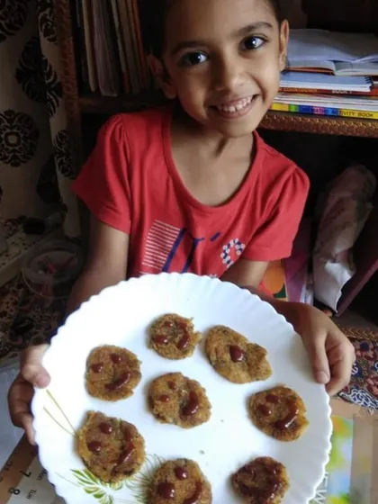 A student's happy face says it all. She is proud of the delicious smiley-faced tikkis she created, turning a simple cooking activity into a creative expression.
