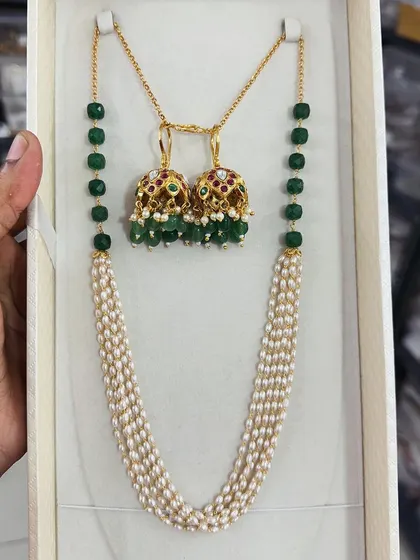 A beautiful combination of green beads and pearls, this set features a multi-strand pearl necklace paired with traditional jhumki earrings. The green beads add a lovely pop of color.